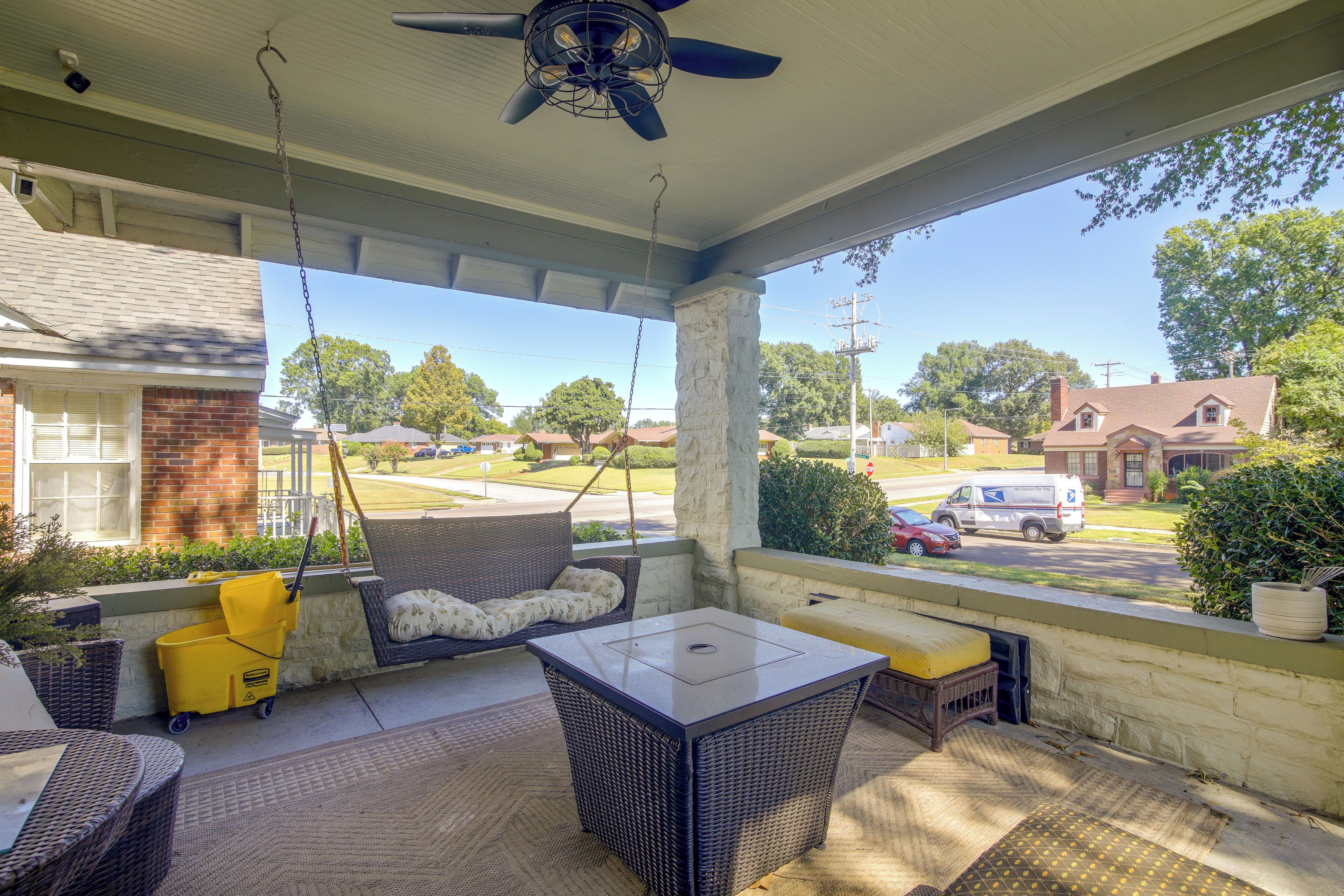 A covered porch with wicker furniture, a swing, and a view of a residential street.