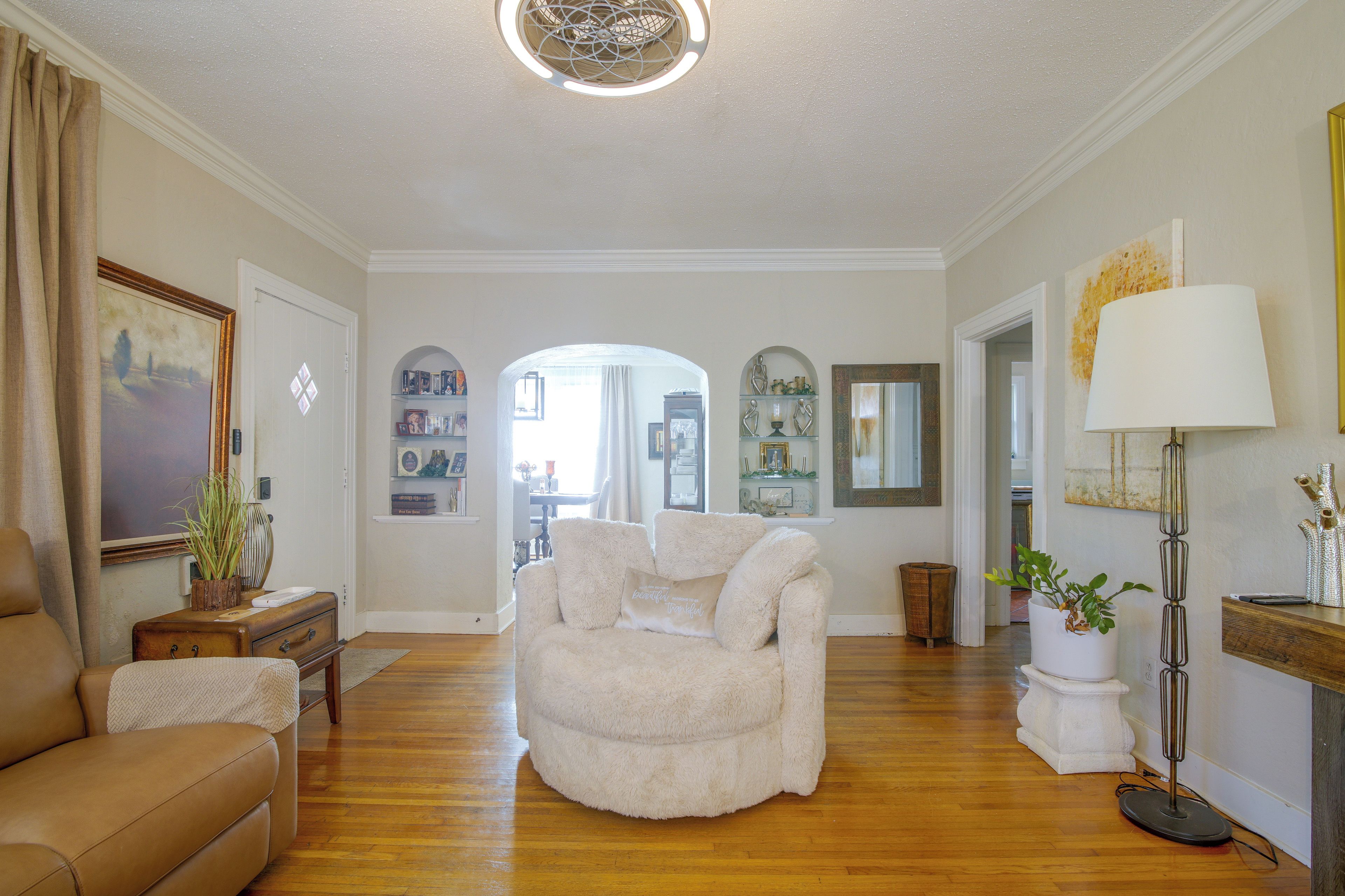 A spacious living room with hardwood flooring, a beige armchair, a brown sofa, and a lamp.