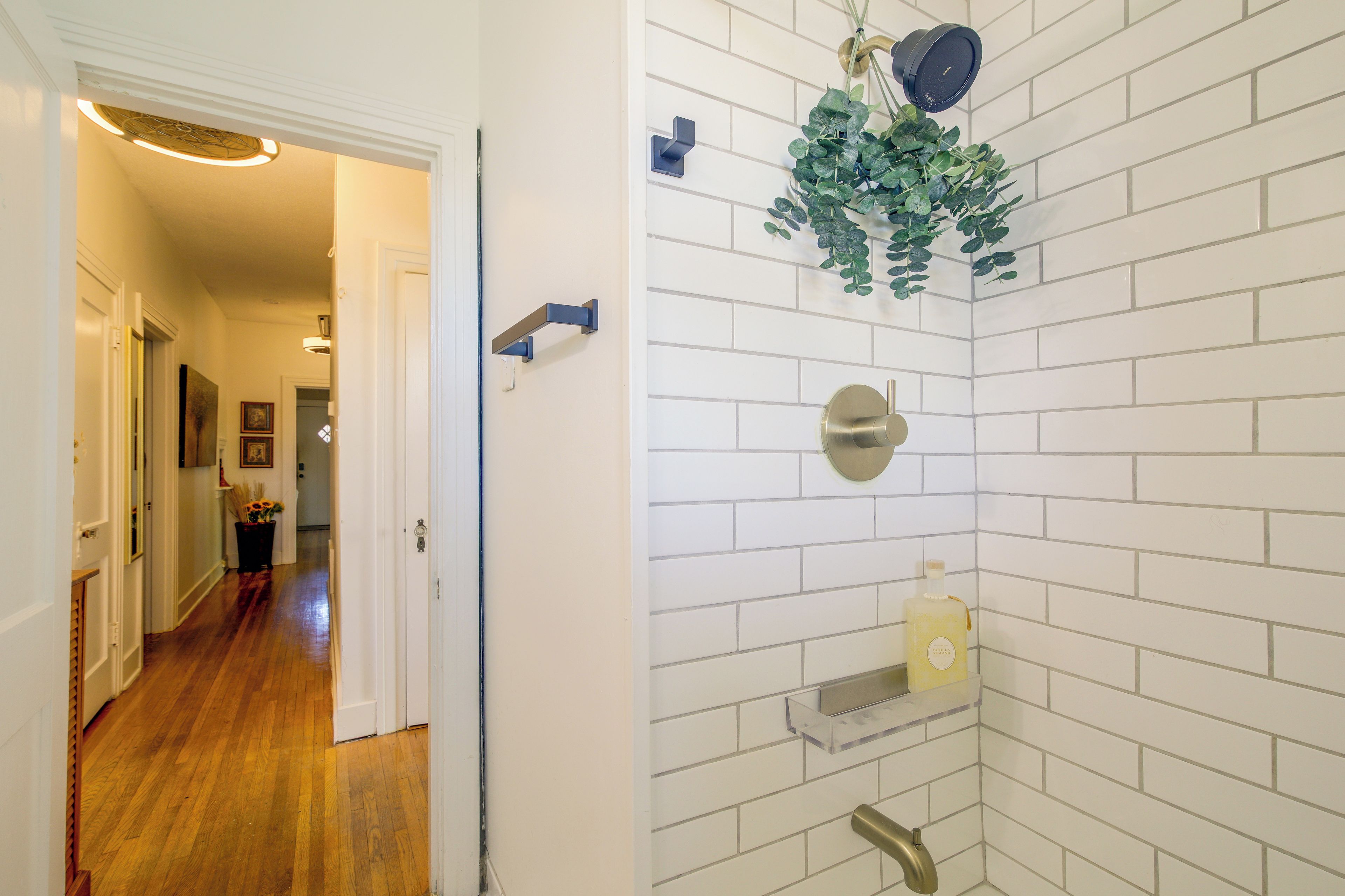 A bathroom with white subway tiles, a shower with a round showerhead, and a clear shelf with a bottle.
