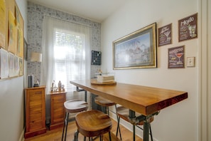 A kitchen with a wooden bar, bar stools, a window with sheer curtains, and wall decorations including a framed cityscape and cocktail posters. - Midtown Memphis Home w/ Home Gym & Office (Memphis)