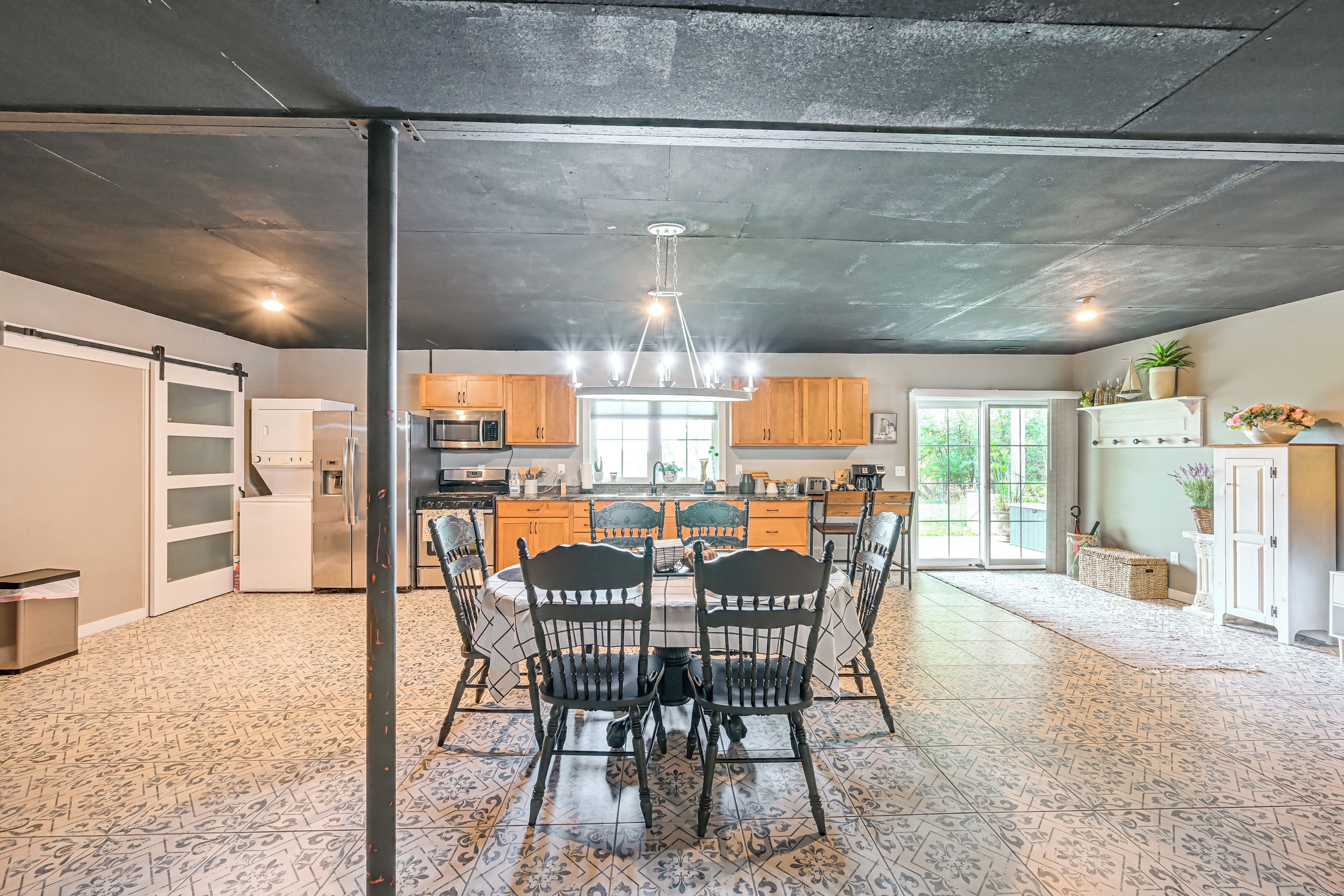A modern kitchen with a dining area, featuring a central island, wooden cabinets, and a large window.