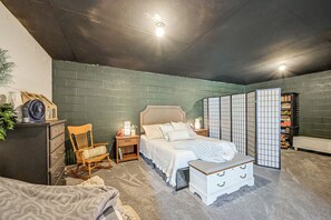 Ein Schlafzimmer mit Bett, Sessel, Nachttisch, Kommode, Bücherregal und Wanddekoration.