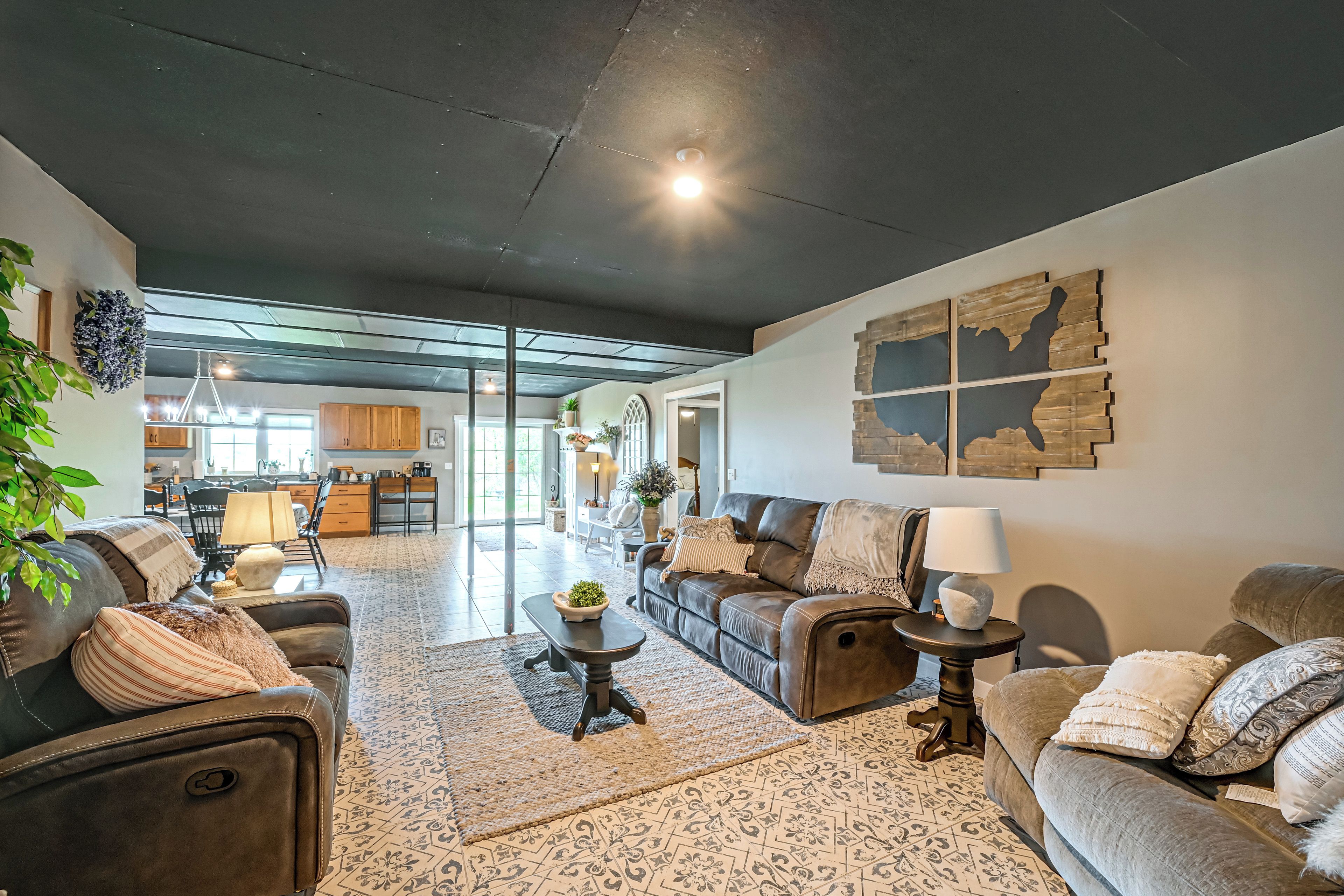 A spacious living room with a sofa set, a coffee table, and a rug. There is a kitchen area in the background with cabinets and a dining table.