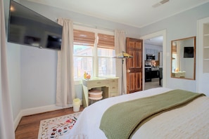 A bedroom with a bed, a desk, a chair, a window with curtains, a television, and a kitchen visible through an open door. - Big Spring 'bison House' w/ Patio & Yard! (Big Spring)