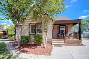 A single-story house with a front porch, a small garden area with mulch, and a clear blue sky. - Big Spring 'bison House' w/ Patio & Yard! (Big Spring)