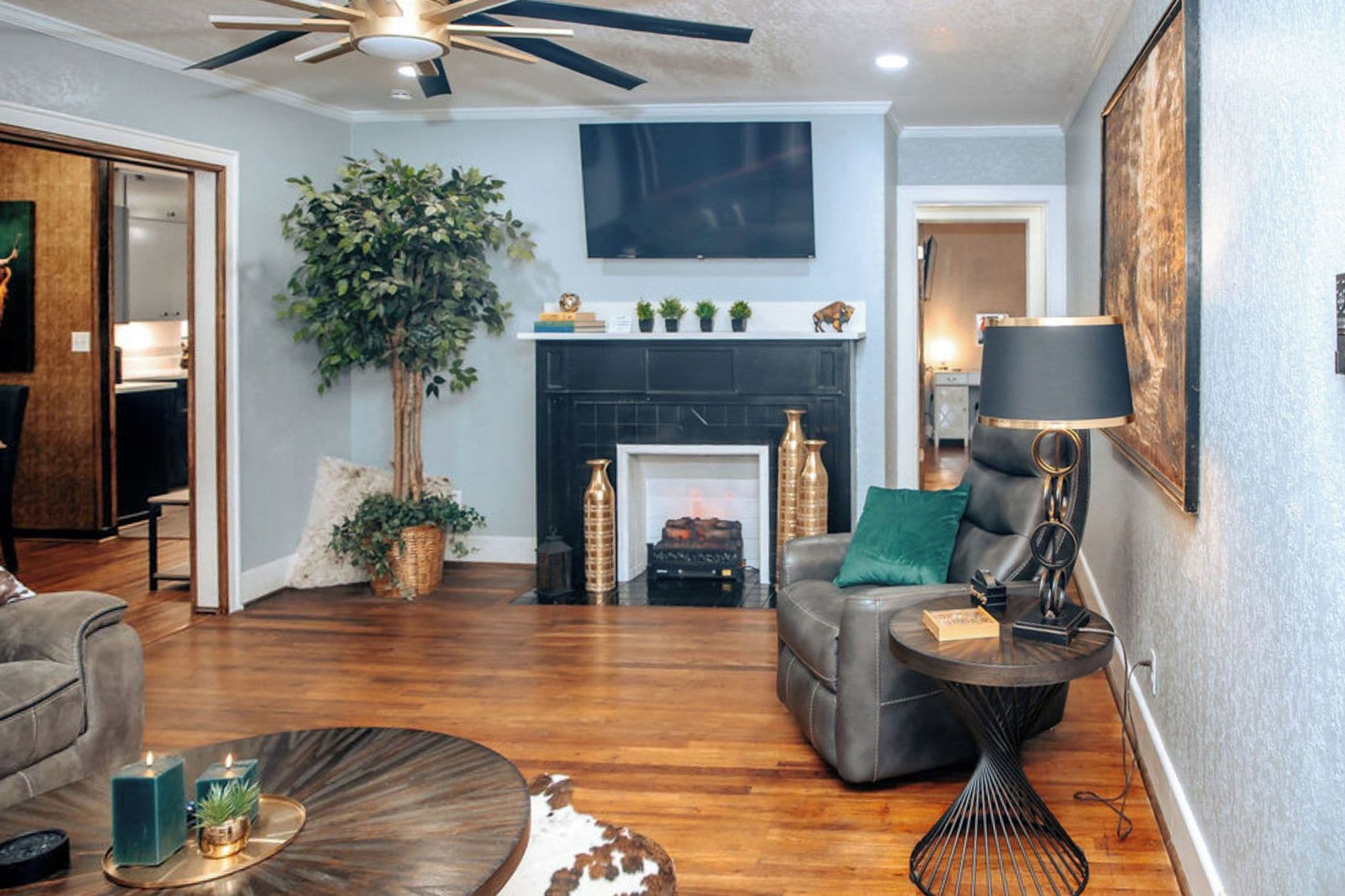 A living room with a fireplace, a ceiling fan, and a television mounted on the wall.