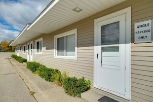 A row of single-story mobile homes with white siding and beige trim. Each unit has a front door and a window, and there is a sign indicating 'ANGLE PARKING ONLY' on the side of one of the homes.