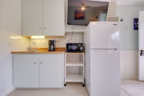 Una cocina compacta con armarios blancos, cafetera, microondas y refrigerador.