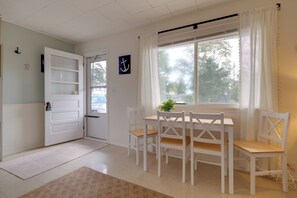 Una habitación con una puerta blanca, una ventana con cortinas, una mesa con sillas y una planta pequeña sobre la mesa.
