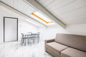 A room with a high ceiling, a skylight, a sofa, a dining table with chairs, and a door. - Cozy Slooping Rooftop (Naples)