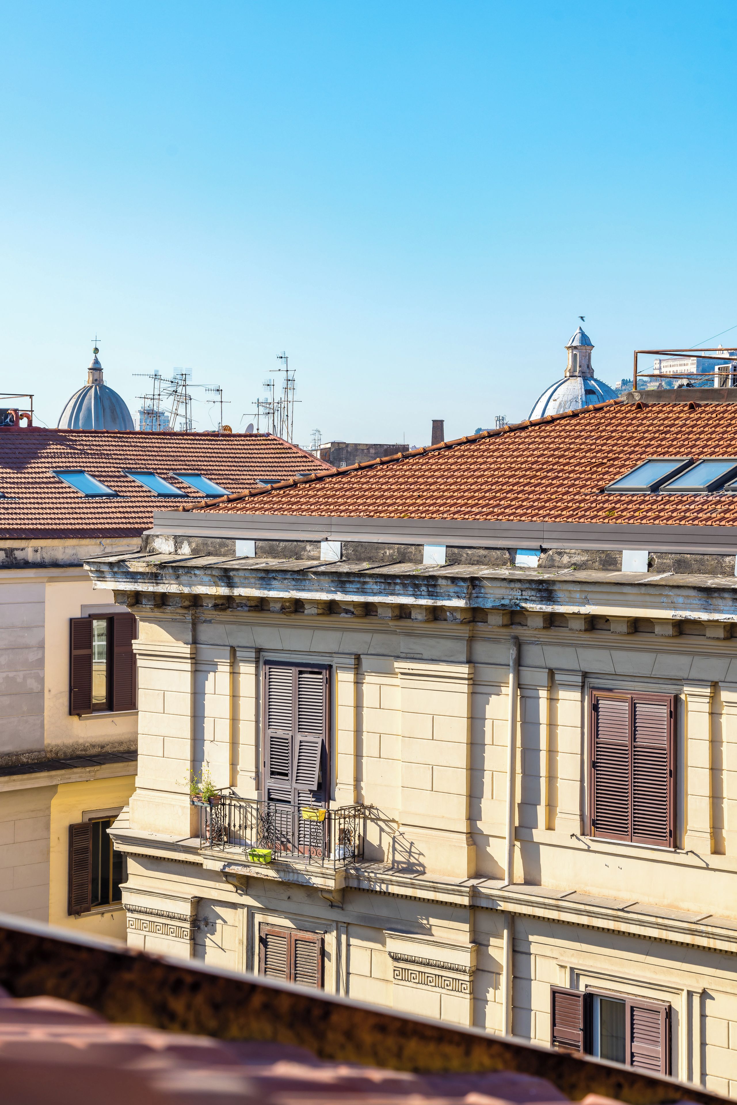 Un bâtiment doté d’un balcon, d’une fenêtre avec des volets et, au fond, d’une structure en forme de dôme.