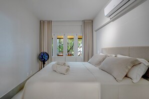 Quarto de hotel com cama, ventoinha e vista para o verde pela janela.