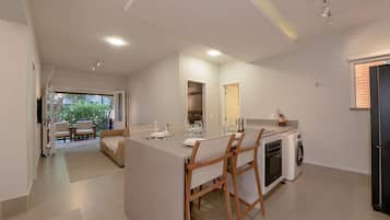 A modern kitchen with a central island, wooden chairs, a built-in oven, and a washing machine.