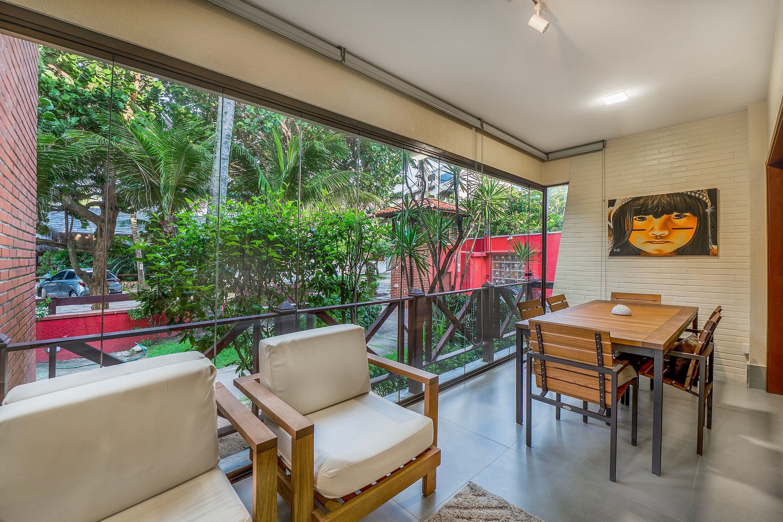 Un interior moderno con un balcón, una zona de comedor con mesa y sillas, y un ventanal que ofrece vistas a zonas verdes y un edificio rojo.