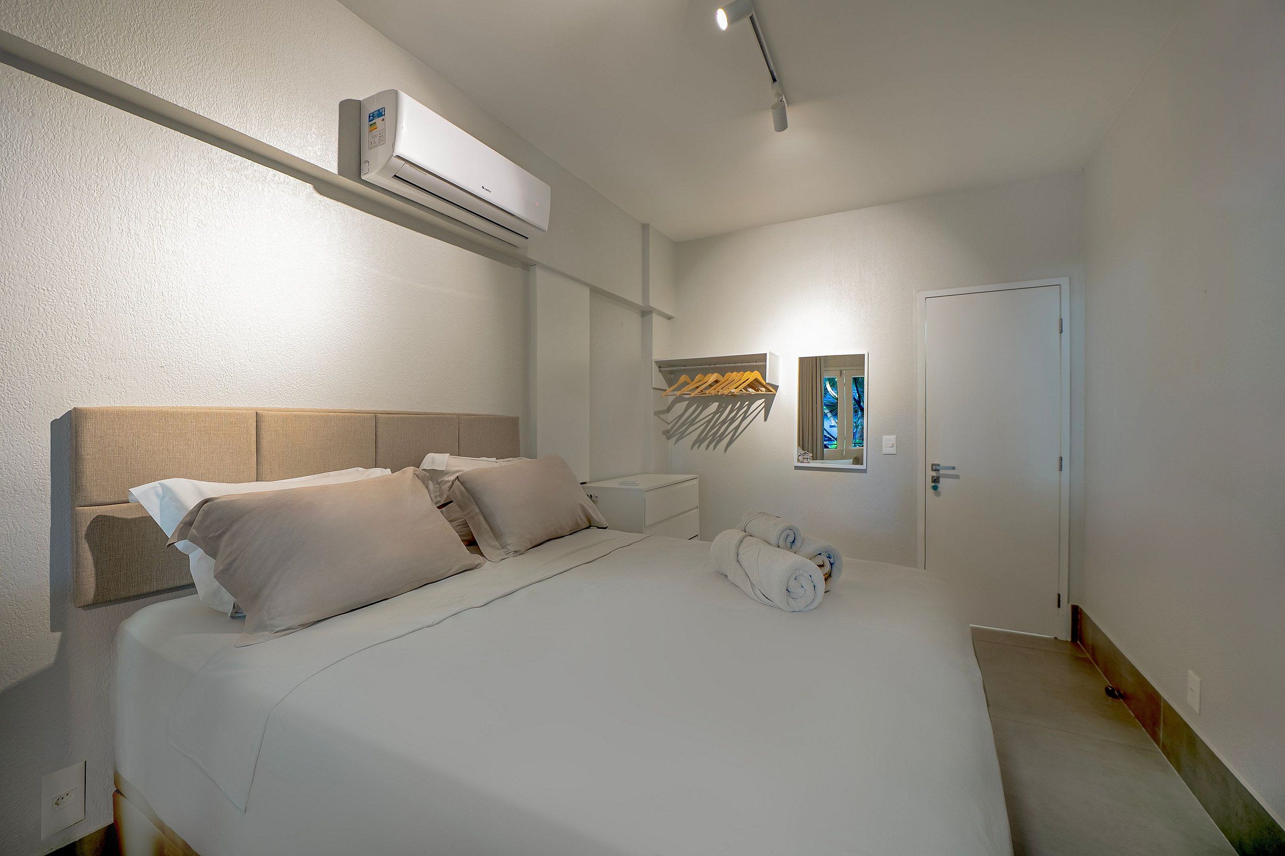Habitación de hotel con cama, aire acondicionado de pared, mesita de noche, espejo y puerta.