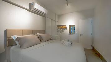 Habitación de hotel con cama, aire acondicionado de pared, mesita de noche, espejo y puerta.