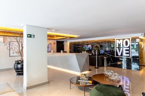 A hotel lobby with a reception desk, a 'MOVE' sign, a potted plant, and a seating area with a table. - Move #801 - Apartment With Balcony by Carpediem (João Pessoa)