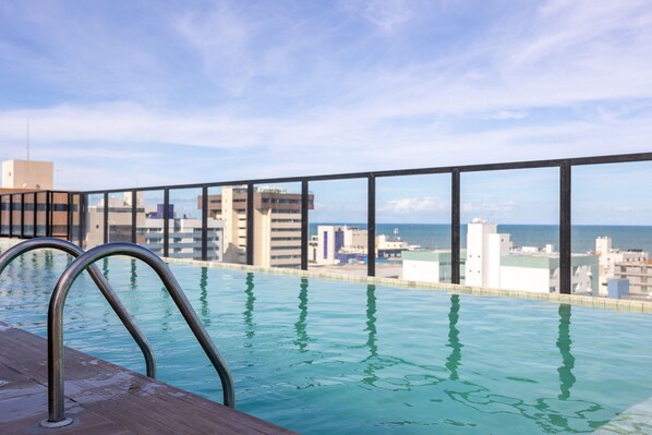 En infinitypool med metallräcken, ett trädäck och utsikt över staden och havet.