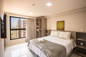 Une chambre d’hôtel comprenant un lit, une fenêtre avec des rideaux, une armoire, une table de chevet et une œuvre d’art accrochée au mur.