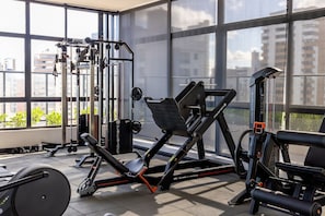 Une salle de sport équipée de divers appareils d’exercice, dotée de grandes fenêtres et offrant une vue sur les bâtiments environnants.