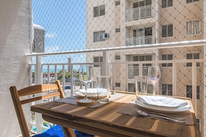 A balcony with a table set for two, a chair, and a view of a building with multiple windows. - Mirante #508 - Apto With 2 Bedrooms by Carpediem (Fortaleza)