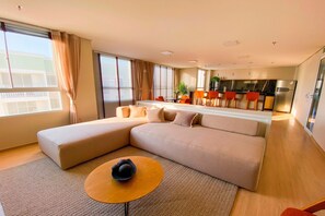 A modern living room with a large sectional sofa, a round coffee table, and a kitchen area in the background. - Mirante #508 - Apto With 2 Bedrooms by Carpediem (Fortaleza)