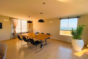 A dining area with a wooden table and black chairs, a potted plant, and a view of the sea through a window. - Mirante #508 - Apto With 2 Bedrooms by Carpediem (Fortaleza)