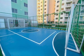 An indoor basketball court with a net, surrounded by a green fence and a building in the background. - Mirante #1108 - Apartment in Fortaleza by Carpediem (Fortaleza)