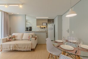 A modern living room with a sofa, a dining table set for two, and a kitchen in the background. - Mirante #1108 - Apartment in Fortaleza by Carpediem (Fortaleza)
