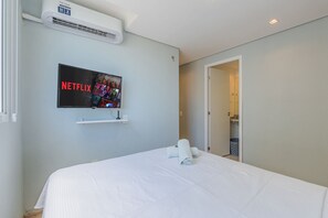 Een hotelkamer met een bed, een tv met het Netflix-logo, een wandairconditioner en een deur naar een badkamer.