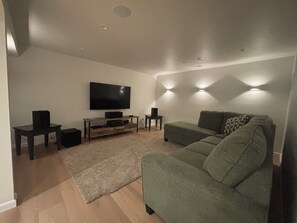 Ein Wohnzimmer mit einem Flachbildfernseher, einem grünen Sofa, einem Holztisch und zwei Beistelltischen.