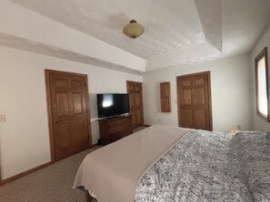 Ein Schlafzimmer mit einem Bett, einem Fernseher auf einer Kommode, Holztüren und einer Deckenleuchte.