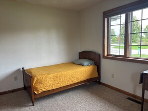 A small, single-bed room with a wooden frame, a yellow bedspread, and a window with a view of a street. - Spacious 4-bedroom house in lovely Neenah- 17 min from EAA (Neenah)