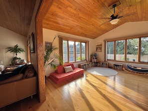 A spacious living room with a wooden ceiling, large windows, a red sofa, a coffee table, and a bookshelf. - Spacious 4-bedroom house in lovely Neenah- 17 min from EAA (Neenah)