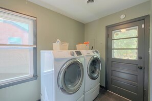 Une buanderie équipée d’un lave-linge et d’un sèche-linge à chargement frontal, d’un panier contenant des articles et d’une porte avec une fenêtre.