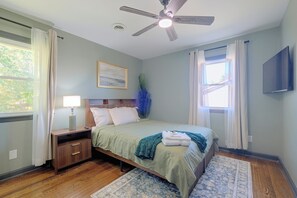 A bedroom with a bed, nightstand, lamp, ceiling fan, artwork, and a window with curtains. - Walk to VSU Campus! Your Escape Away From Home (Petersburg)