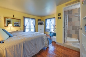 Un dormitorio con cama, escritorio, ducha y ventana con cortinas.