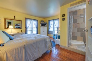 Un dormitorio con cama, escritorio, ducha y ventana con cortinas.