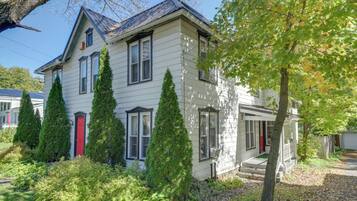 Une maison à deux étages avec une porte rouge, de nombreuses fenêtres et un porche à l’avant.