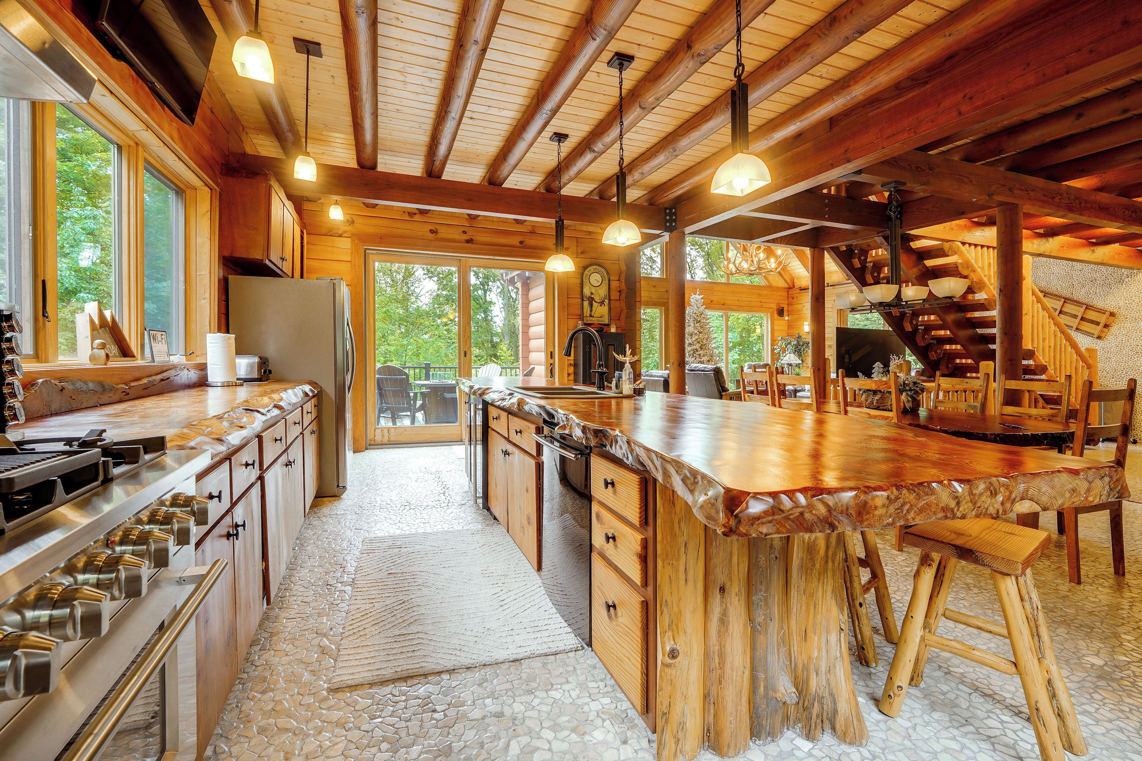 A spacious kitchen with a large island, wooden cabinetry, and a stone-tiled floor.
