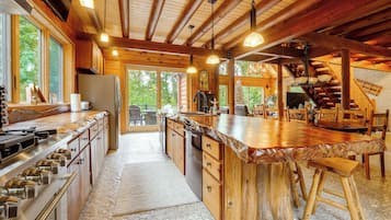 A spacious kitchen with a large island, wooden cabinetry, and a stone-tiled floor.