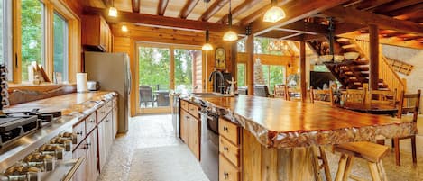 A spacious kitchen with a large island, wooden cabinetry, and a stone-tiled floor.
