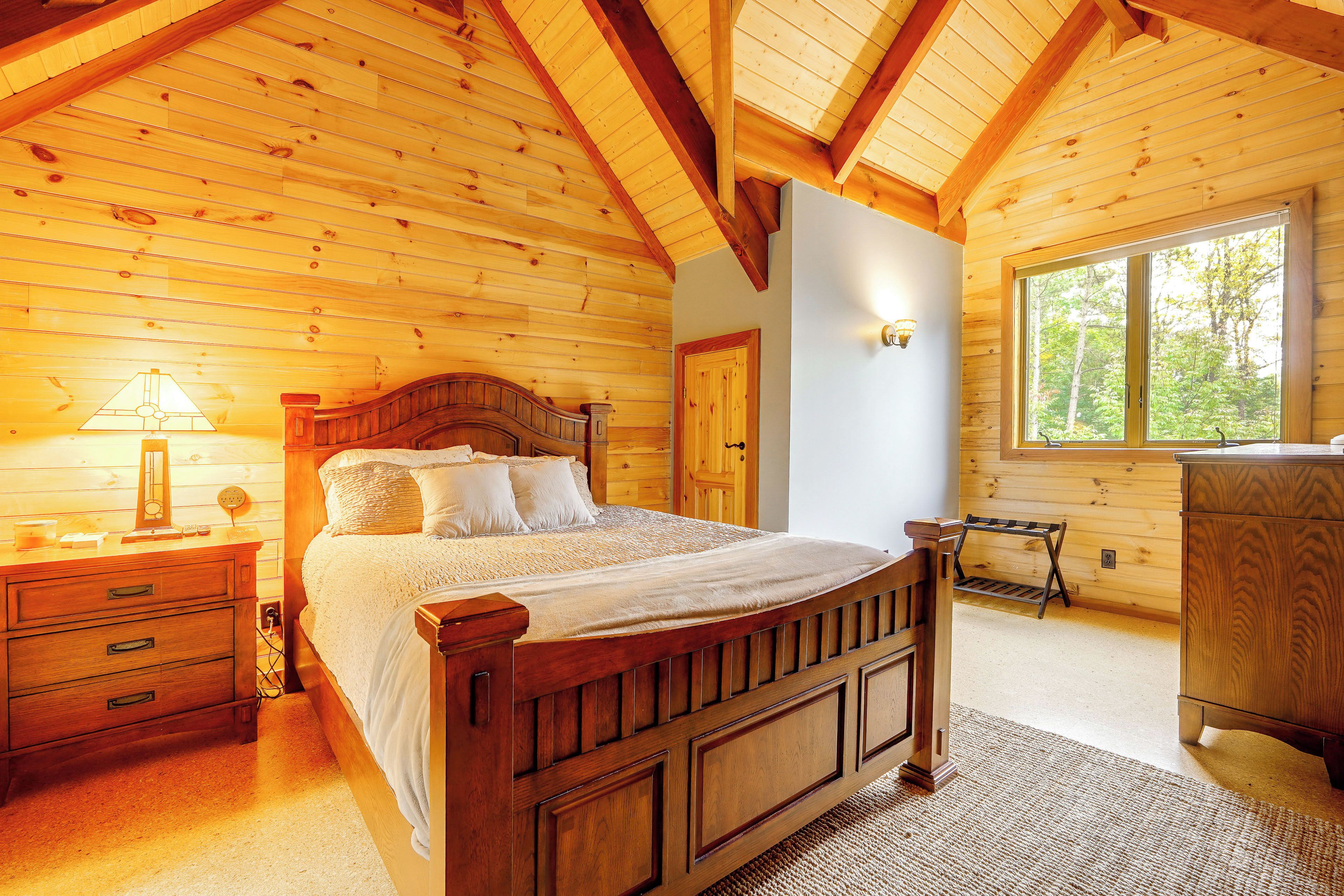 A wooden bedroom with a bed, nightstands, a dresser, and a window with a view of trees.