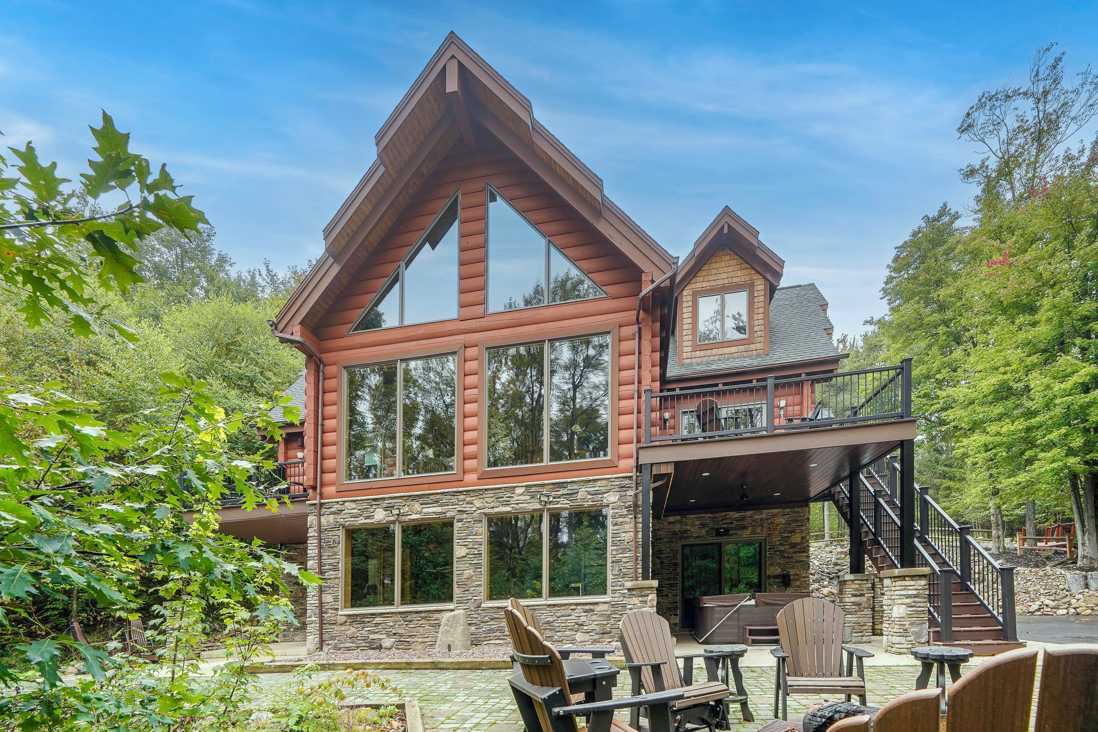 A two-story log cabin with a stone foundation, large windows, and a balcony.