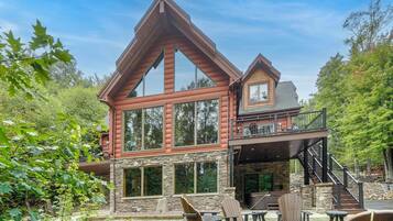 A two-story log cabin with a stone foundation, large windows, and a balcony.