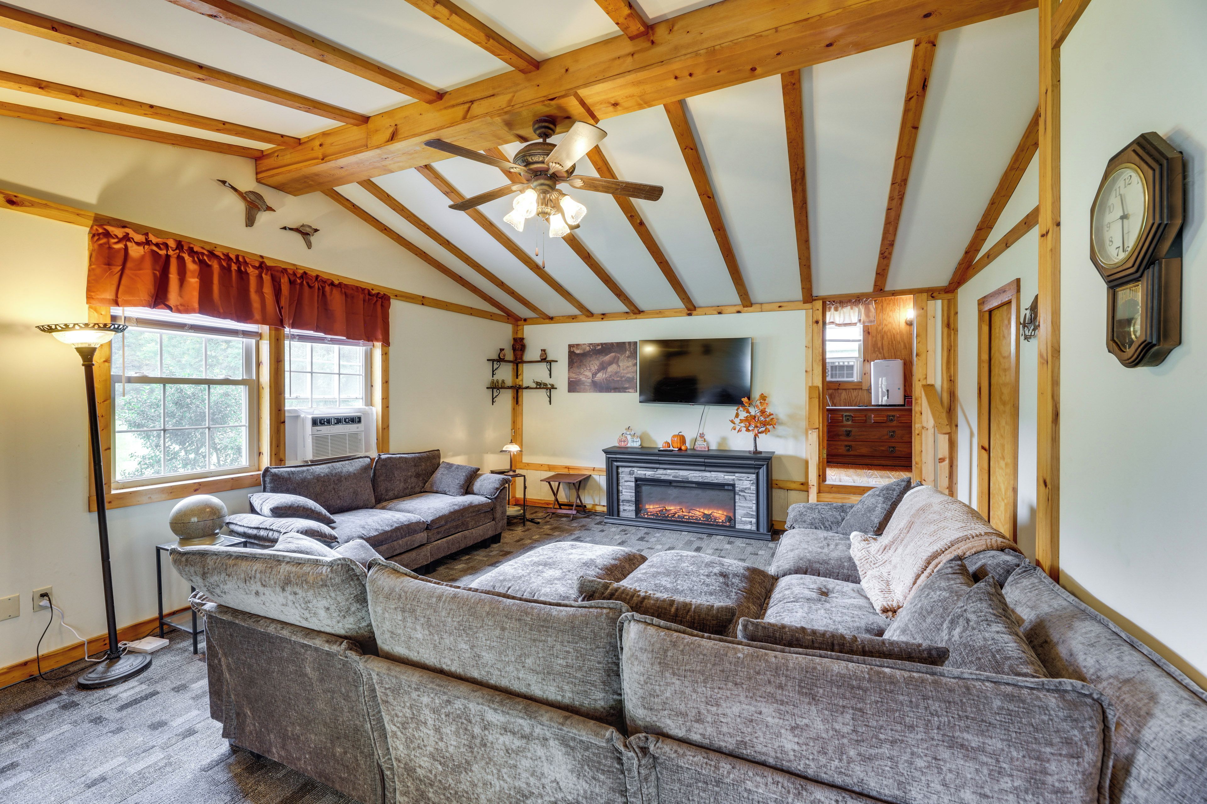 A cozy living room with a sectional sofa, a fireplace, a ceiling fan, and a clock on the wall.