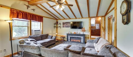 A cozy living room with a sectional sofa, a fireplace, a ceiling fan, and a clock on the wall.