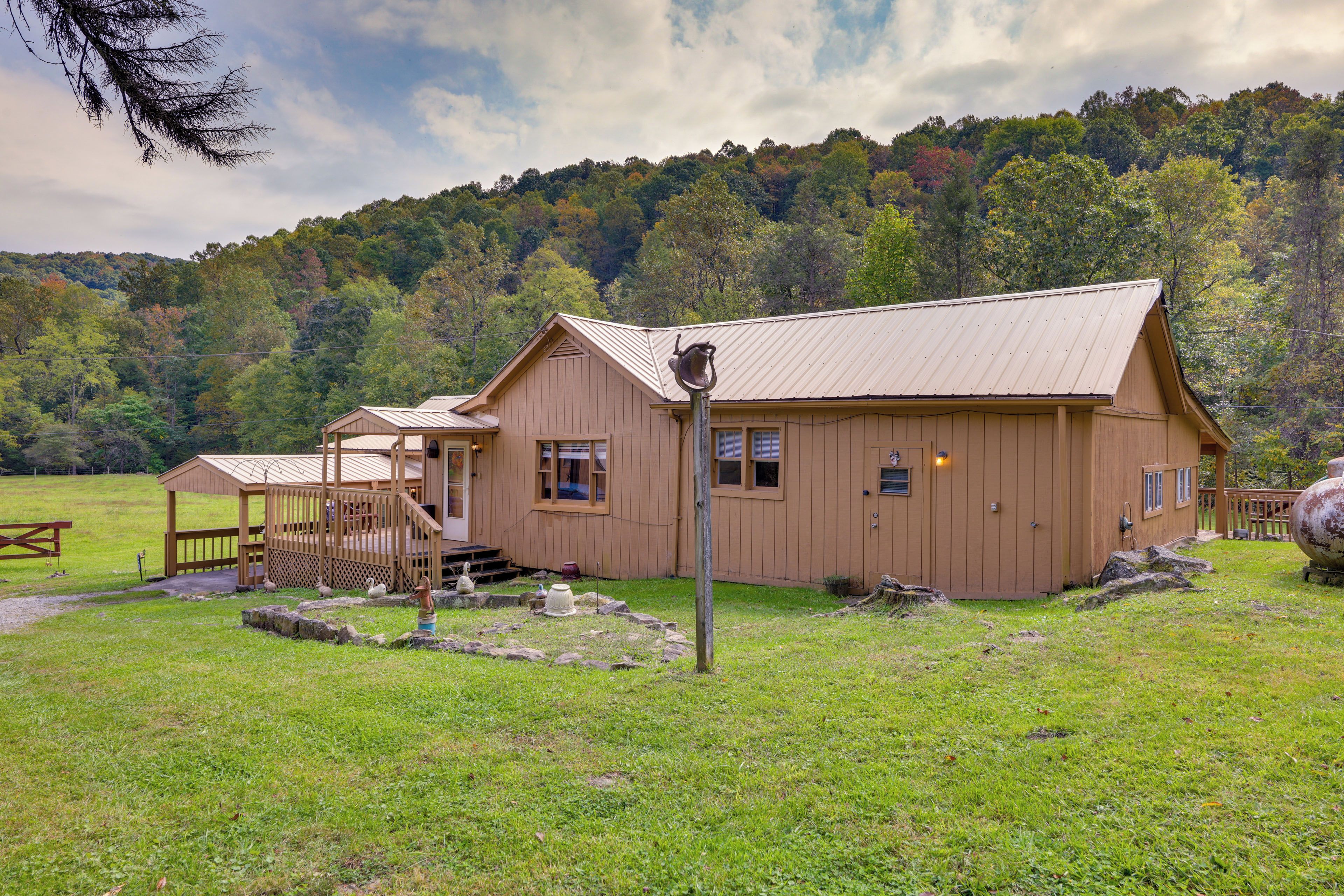 A wooden cabin with a metal roof, situated in a grassy field with a forested hill in the background.