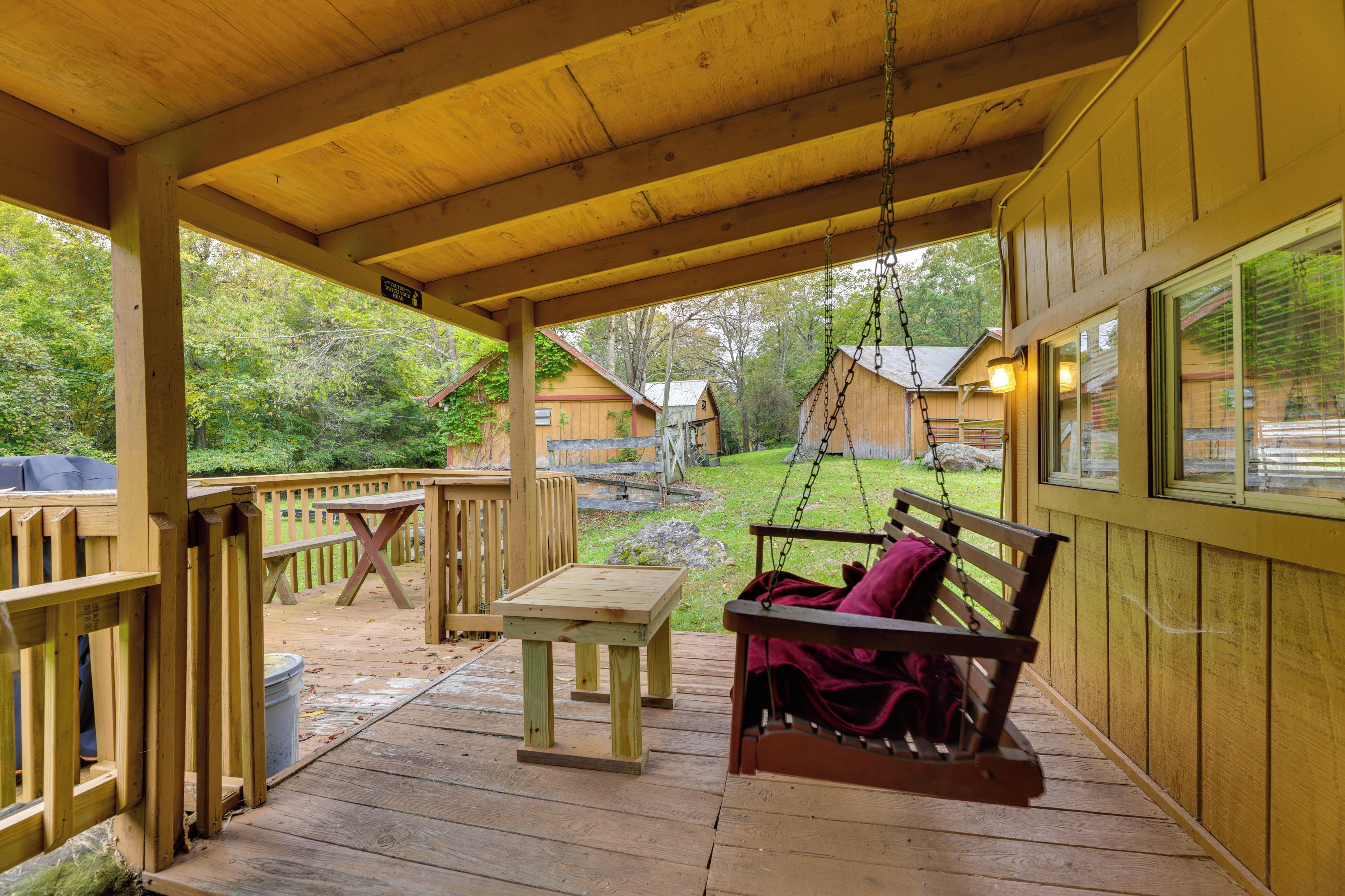 A wooden deck with a swing, picnic table, and a view of a wooded area.