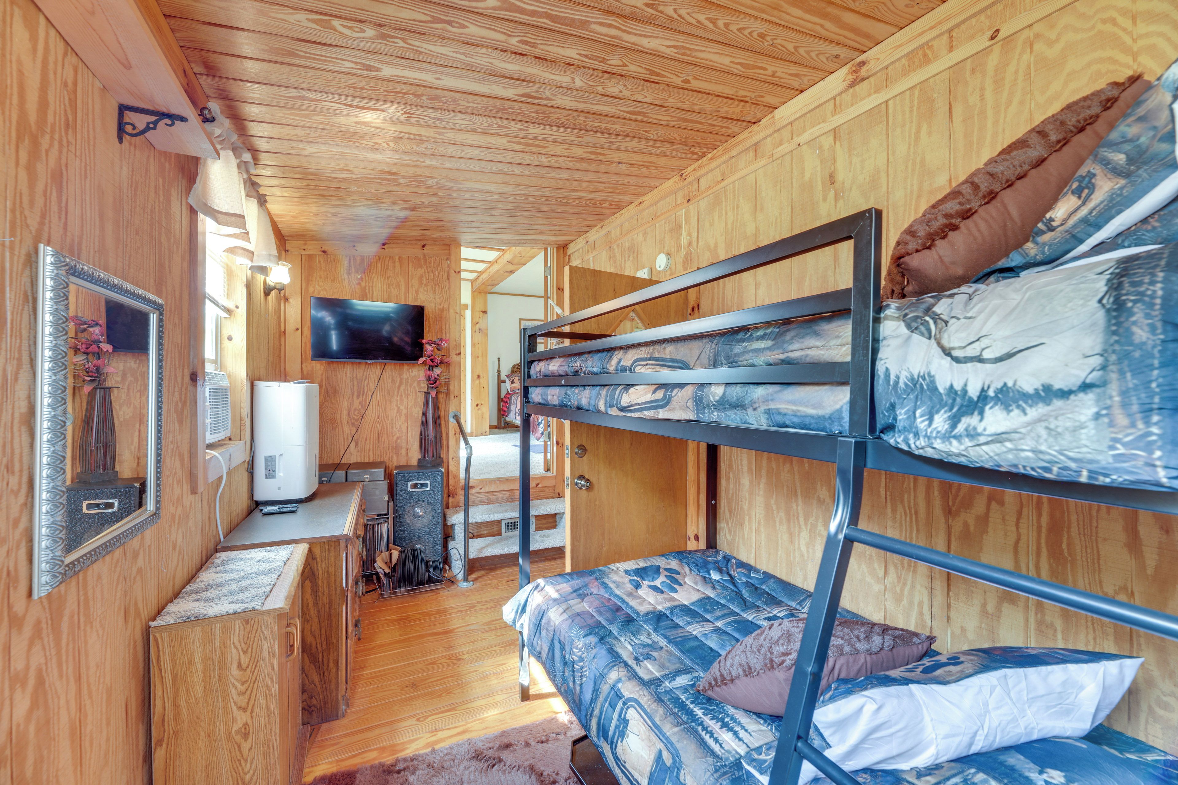 A bunk bed with a mountain-themed bedding, a television mounted on the wall, and a wooden interior.